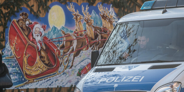 Ein Polizeiauto steht vor einer Weihnachtsmarktbude mit buntem Weihnachtsmann-Motiv Ein Polizeiauto steht vor einer Weihnachtsmarktbude mit buntem Weihnachtsmann-Motiv