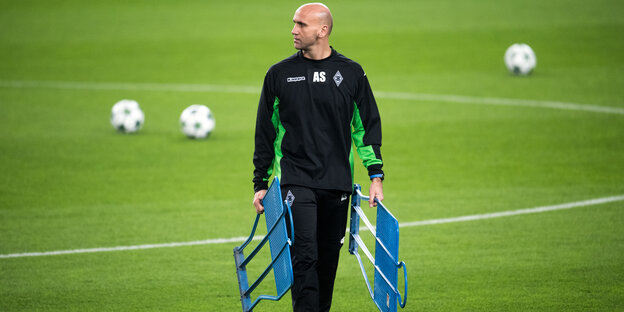 Ein glatzköpfiger Mann im Trainingsanzug geht über ein Fußballfeld Ein glatzköpfiger Mann im Trainingsanzug geht über ein Fußballfeld
