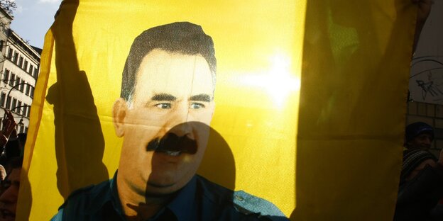Jemand hält eine Fahne mit dem Porträt von Abdullah Öcalan in die Höhe Jemand hält eine Fahne mit dem Porträt von Abdullah Öcalan in die Höhe