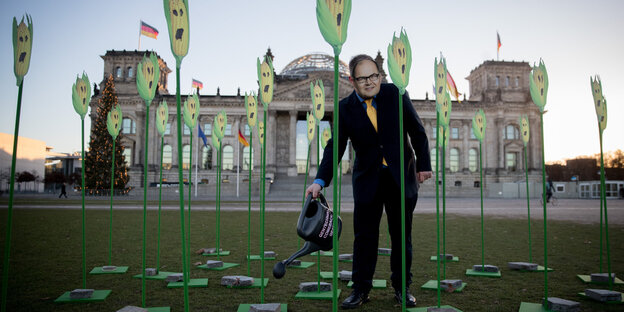 Vor dem Reichstag sind Maispflanzen aus Pappe aufgestellt, ein Aktivist im Anzug hält eine Gießkanne an eine von ihnen Vor dem Reichstag sind Maispflanzen aus Pappe aufgestellt, ein Aktivist im Anzug hält eine Gießkanne an eine von ihnen