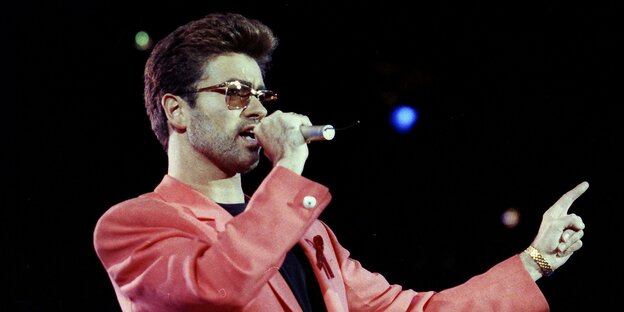 George Michael steht 1992 im roten Sakko auf der Bühne George Michael steht 1992 im roten Sakko auf der Bühne