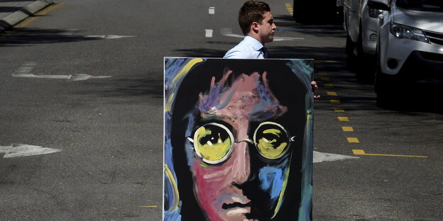 Ein Mann trägt ein psychedelisch buntes Porträt John Lennons über eine Straße Ein Mann trägt ein psychedelisch buntes Porträt John Lennons über eine Straße