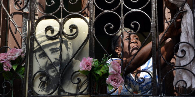 Eine Frau hinter dem Gitter eines Balkons, an das ein Foto von Fidel Castro gelehnt ist Eine Frau hinter dem Gitter eines Balkons, an das ein Foto von Fidel Castro gelehnt ist