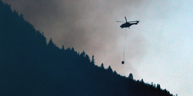 Ein Hubschrauber fliegt über einen Wald und hinein in den Rauch eines Feuers