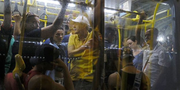 Fahrgäste in einem öffentlichen Bus in Rio de Janeiro durch das Fenster des Busses gesehen. Der Bus ist voll, viele Menschen müssen stehen.