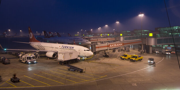 Flugzeugen stehen in der Dämmerung aufgereiht auf einem Flughafen. Gangways sind an ihnen befestigt. Autos befinden sich auf der Fahrbahn Flugzeugen stehen in der Dämmerung aufgereiht auf einem Flughafen. Gangways sind an ihnen befestigt. Autos befinden sich auf der Fahrbahn