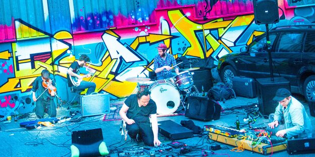 Eine experimentelle Rockband spielt vor einer mit Graffiti bemalten Wand Eine experimentelle Rockband spielt vor einer mit Graffiti bemalten Wand