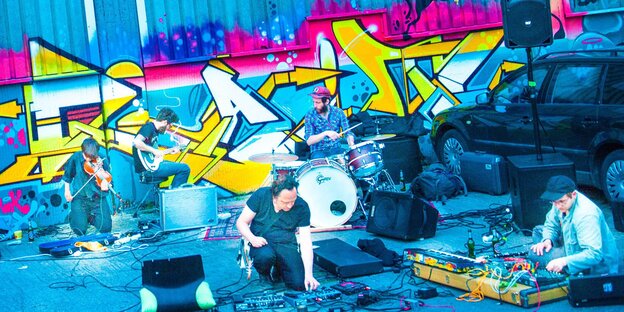 Eine experimentelle Rockband spielt vor einer mit Graffiti bemalten Wand