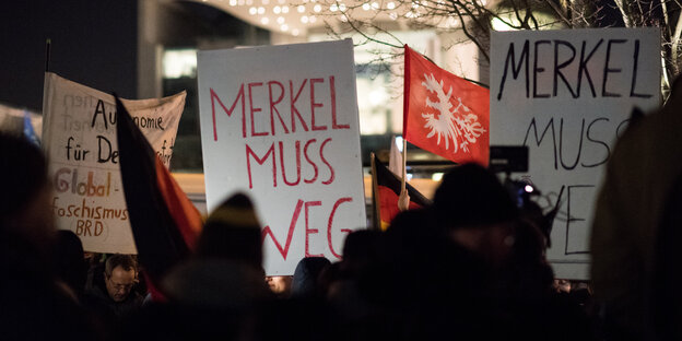 Menschen im Dunkeln. Sie halten Schilder in die Höhe, auf denen steht: „Merkel muss weg" Menschen im Dunkeln. Sie halten Schilder in die Höhe, auf denen steht: „Merkel muss weg"