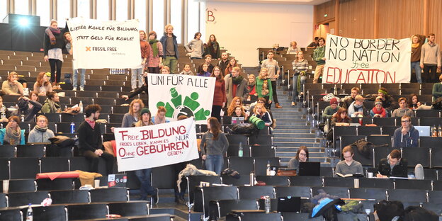 Studenten sitzen und stehen in einem Hörsaal. Sie halten Transparente gegen die geplante Studiengebühr in die Luft. Studenten sitzen und stehen in einem Hörsaal. Sie halten Transparente gegen die geplante Studiengebühr in die Luft.