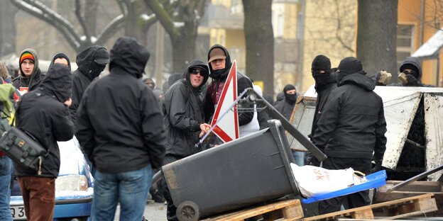 Autonome errichten eine Straßenblockade aus Möbeln und Holz. In der Bildmitte hinter der Blockade stehen zwei vermummte Männer, die sich umamarmen. Autonome errichten eine Straßenblockade aus Möbeln und Holz. In der Bildmitte hinter der Blockade stehen zwei vermummte Männer, die sich umamarmen.