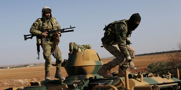 Kämpfer in Tarnkleidung stehen auf einem Militärfahrzeug Kämpfer in Tarnkleidung stehen auf einem Militärfahrzeug