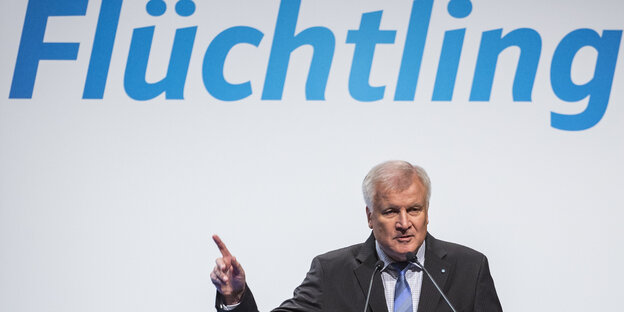 Seehofer zeigt auf den Schriftzug Flüchtling