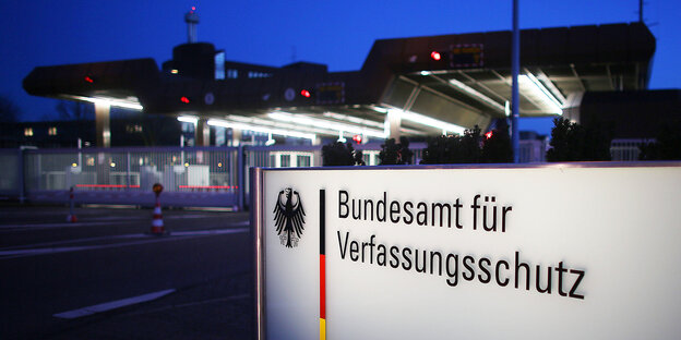Eingang des Bundesamts für Verfassungsschutz bei Dunkelheit, Behördenschild im Vordergrund angeleuchtet Eingang des Bundesamts für Verfassungsschutz bei Dunkelheit, Behördenschild im Vordergrund angeleuchtet
