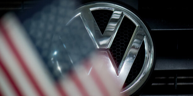 Ein VW-Logo mit davorhängender, unscharfer USA-Flagge