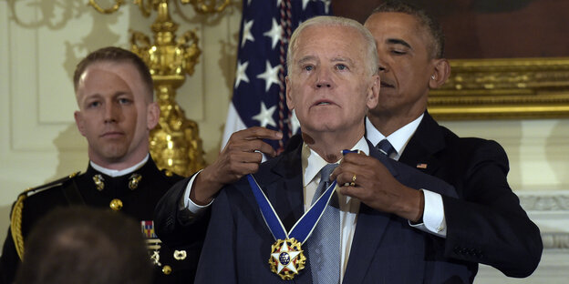 Obama steht hinter Biden und legt ihm die Medaille um den Hals Obama steht hinter Biden und legt ihm die Medaille um den Hals