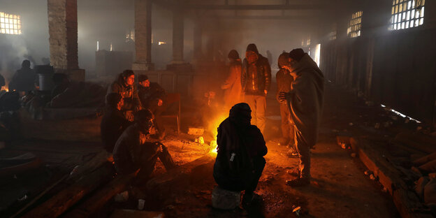 Menschen an einem offenen Feuer in einer Halle Menschen an einem offenen Feuer in einer Halle