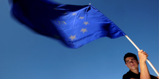 Ein junger Mann hält eine EU-Flagge vor blauem Himmel. Ein junger Mann hält eine EU-Flagge vor blauem Himmel.