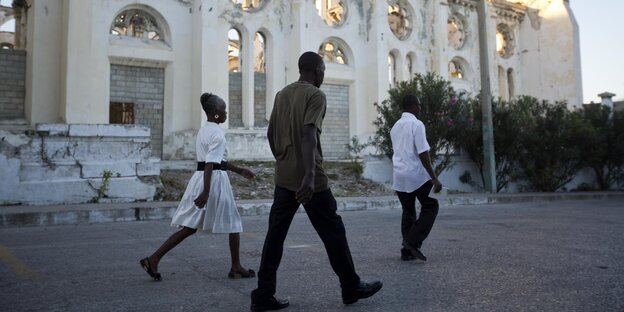 Drei Menschen laufen an der Ruine einer Kathedrale in Port-au-Prince, Haiti, vorbei Drei Menschen laufen an der Ruine einer Kathedrale in Port-au-Prince, Haiti, vorbei