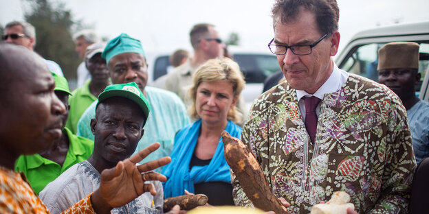 Gerd Müller hält Holzstücke in den Händen und trägt ein buntes Oberteil, neben ihm stehen nigerianische Bauern Gerd Müller hält Holzstücke in den Händen und trägt ein buntes Oberteil, neben ihm stehen nigerianische Bauern