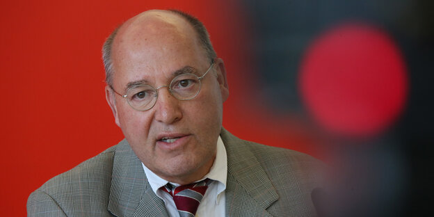 Gregor Gysi sitzt in grauem Anzug vor einer roten Wand