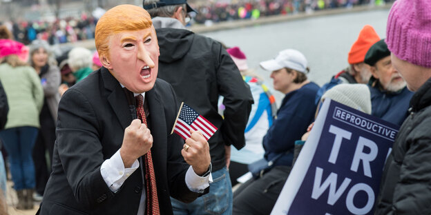 Ein Mensch trägt bei einer Demonstration eine Trump-Maske mit verlängerter Nase