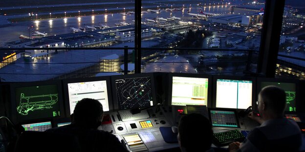 Menschen blicken auf Bildschirme und einen Flughafen