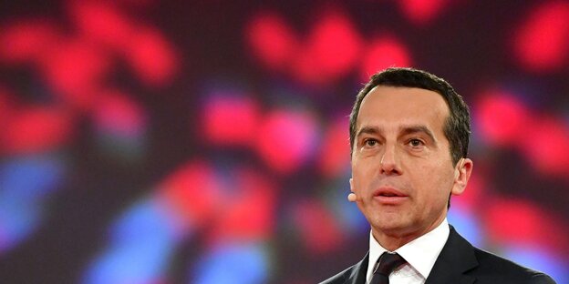 Christian Kern steht vor einer Wand aus roten und blauen Lichtern