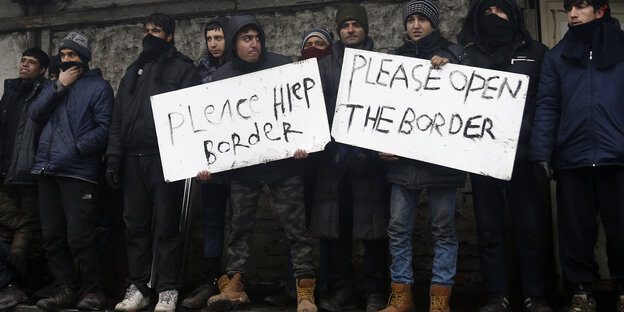Männer stehen draußen und halten Schilder hoch. Auf einem steht: „Please open the border". Männer stehen draußen und halten Schilder hoch. Auf einem steht: „Please open the border".