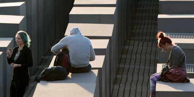 drei Menschen sitzen, jeder für sich, auf Stelen des Denkmals für die ermordeten Juden Europas drei Menschen sitzen, jeder für sich, auf Stelen des Denkmals für die ermordeten Juden Europas