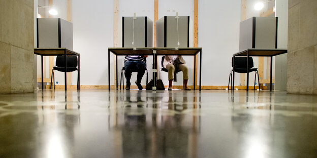 Vier Wahlkabinen, man erkennt, dass nur die beiden mittleren besetzt sind Vier Wahlkabinen, man erkennt, dass nur die beiden mittleren besetzt sind
