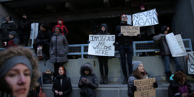 Menschen in New York halten Schilder hoch: Never Again und Immigrants are welcome here, steht darauf Menschen in New York halten Schilder hoch: Never Again und Immigrants are welcome here, steht darauf