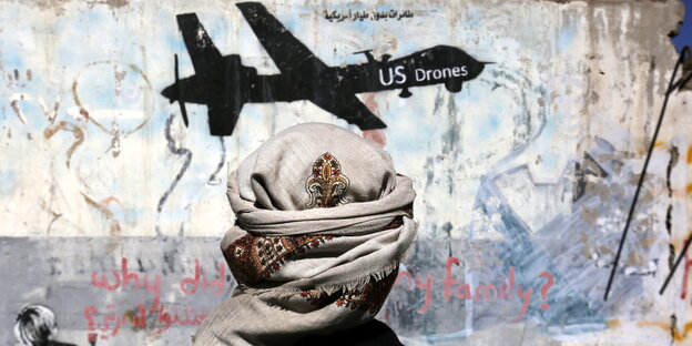 Ein Mann mit Turban vor einer Wand, auf die eine schwarze US-Drohne gemalt ist Ein Mann mit Turban vor einer Wand, auf die eine schwarze US-Drohne gemalt ist