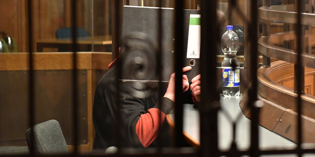 Angeklagter versteckt sich hinter einem Aktenordner Angeklagter versteckt sich hinter einem Aktenordner