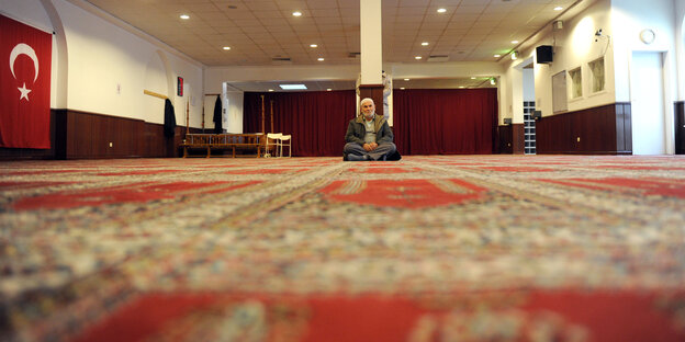 Ein Mann sitzt in einer Moschee auf Teppichen Ein Mann sitzt in einer Moschee auf Teppichen
