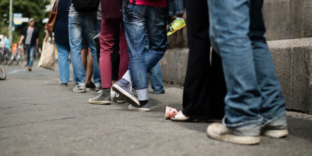 Menschen stehen in einer langen Schlange, man sieht nur die Beine, die sich aneinanderreihen Menschen stehen in einer langen Schlange, man sieht nur die Beine, die sich aneinanderreihen