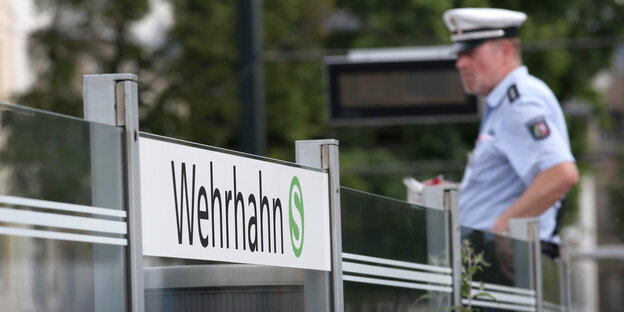 Ein Polizist steht neben einem Schild, auf dem "Wehrhahn" steht Ein Polizist steht neben einem Schild, auf dem "Wehrhahn" steht