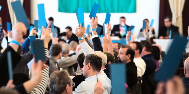 Menschen sitzen in einem Saal und halten blaue Karten hoch Menschen sitzen in einem Saal und halten blaue Karten hoch