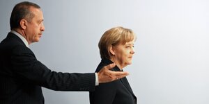 Erdogan streckt den rechten Arm aus und weist Angela Merkel, die vor ihm geht, den Weg