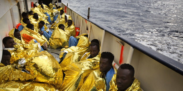 Gerettete Flüchtlinge sitzen in goldene Wärmedecken gehüllt auf einem Boot Gerettete Flüchtlinge sitzen in goldene Wärmedecken gehüllt auf einem Boot