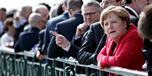 Angela Merkel lehnt gegen einen Zaun und ist von anderen Menschen umringt Angela Merkel lehnt gegen einen Zaun und ist von anderen Menschen umringt