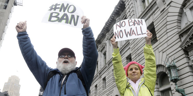 Zwei Menschen halten Plakate in die Höhe, auf denen "No ban, no wall" steht Zwei Menschen halten Plakate in die Höhe, auf denen "No ban, no wall" steht