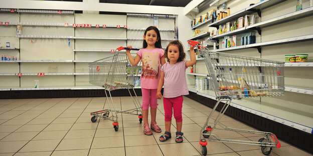 Zwei Mädchen in rosa Leggind und rosa T-Shirts stehen in einem Supermarkt, jede hat einen Einkaufswagen an der Hand Zwei Mädchen in rosa Leggind und rosa T-Shirts stehen in einem Supermarkt, jede hat einen Einkaufswagen an der Hand