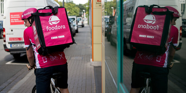 Ein Foodora-Lieferant mit Rucksack fährt Rad. Er spiegelt sich in einem Schaufenster Ein Foodora-Lieferant mit Rucksack fährt Rad. Er spiegelt sich in einem Schaufenster