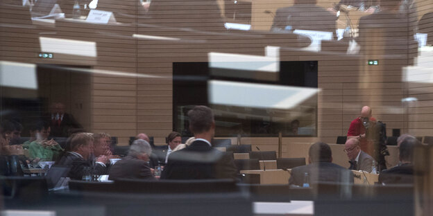 Männer, die in einem Saal sitzen, sind durch ein Fenster sichtbar Männer, die in einem Saal sitzen, sind durch ein Fenster sichtbar