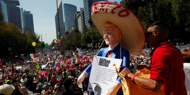 Eine Figur des US-Präsidenten Trump mit Sombrero und Hitler-Schild vor einer Menge Demonstranten Eine Figur des US-Präsidenten Trump mit Sombrero und Hitler-Schild vor einer Menge Demonstranten