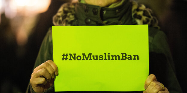 Frau hält gelbes Schild hoch mit Hashtag #NoMuslimBan Frau hält gelbes Schild hoch mit Hashtag #NoMuslimBan