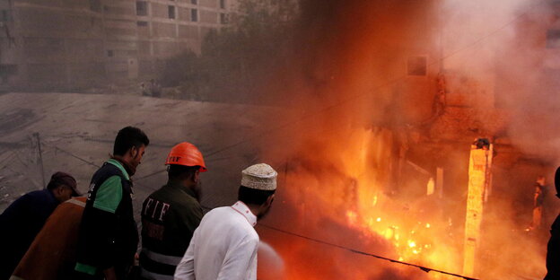 In Karachi brennt ein Medikamenten-Depot lichterloh, Menschen stehen ratlos daneben In Karachi brennt ein Medikamenten-Depot lichterloh, Menschen stehen ratlos daneben