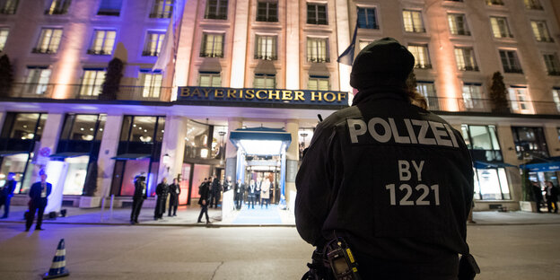 Ein Polizist steht vor dem in der Dunkelheit violett und gelb erleuchteten Hotel Bayerischer Hof in München Ein Polizist steht vor dem in der Dunkelheit violett und gelb erleuchteten Hotel Bayerischer Hof in München
