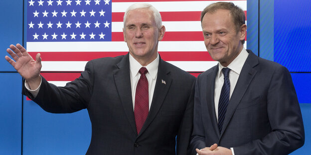 Zwei Männer in Anzügen stehen vor einer US-amerikanischen Flagge Zwei Männer in Anzügen stehen vor einer US-amerikanischen Flagge